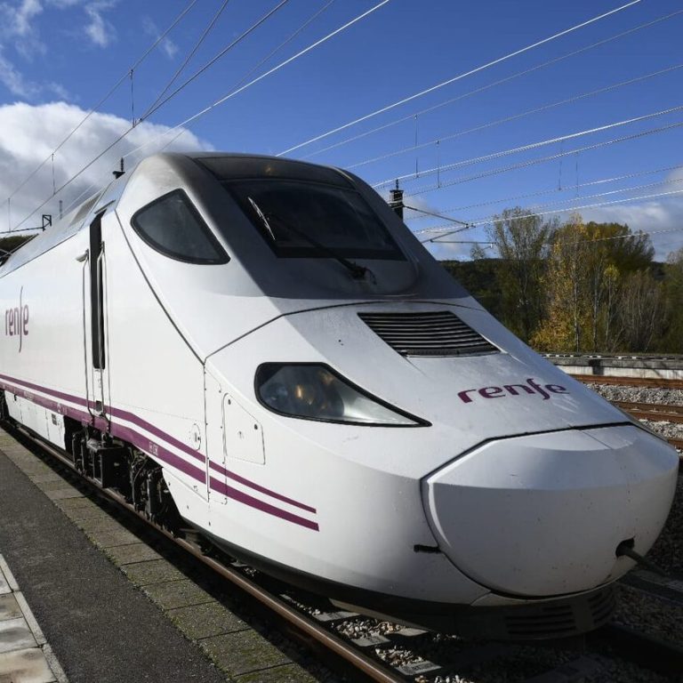 AVE de Renfe en una estación, con cielo azul y nubes al fondo.